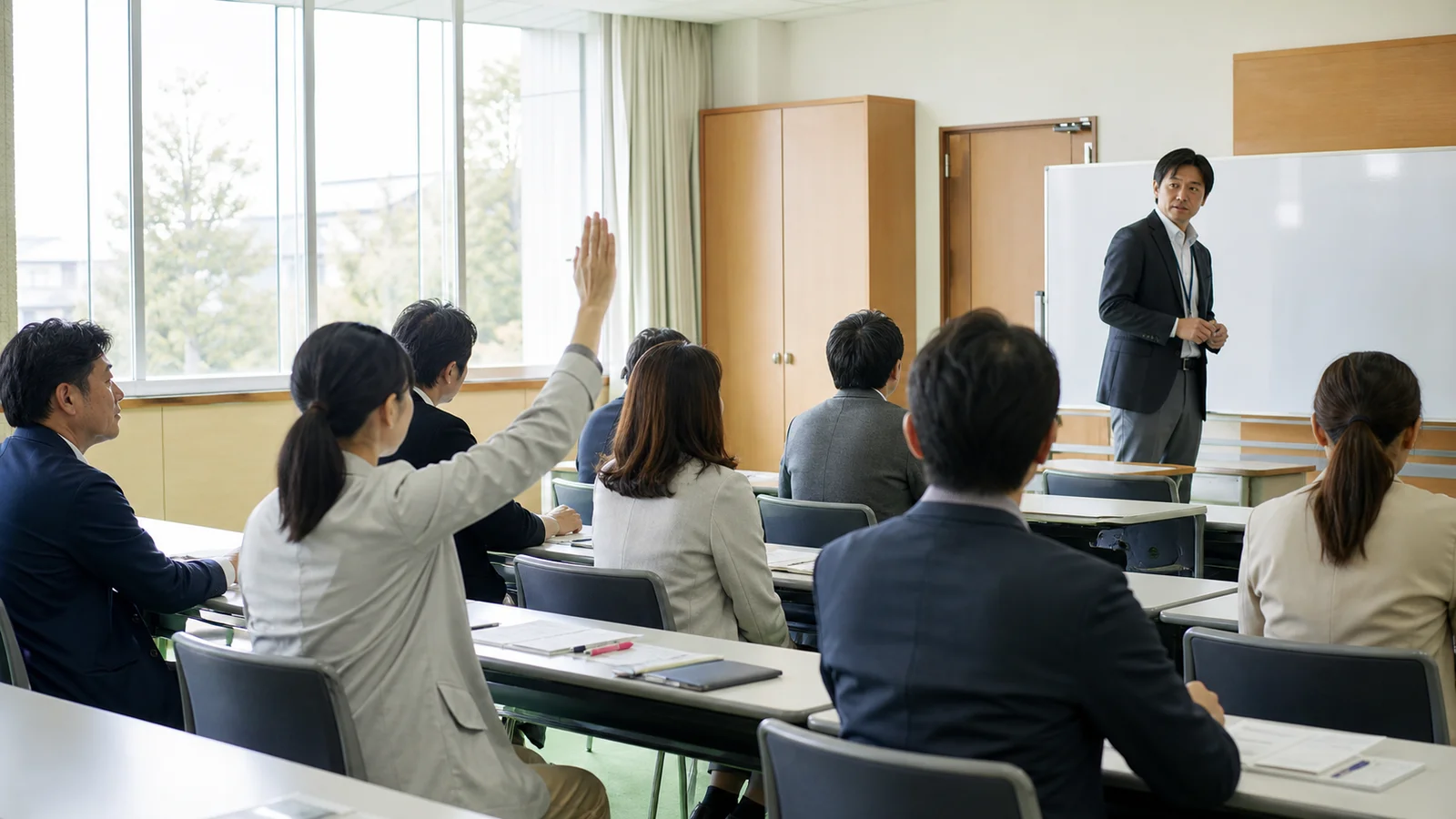 研修中に手を挙げて質問する教職員と、そちらを向いた講師